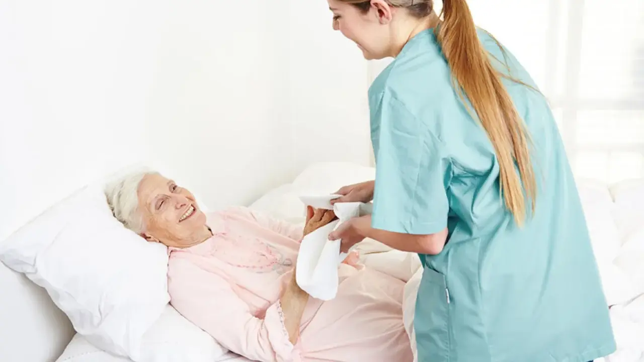 Opiekunka delikatnie myje krocze starszej pacjentce, która uśmiecha się z wdzięcznością.