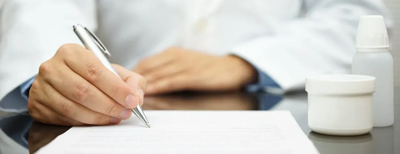 Lekarz pisze receptę farmaceutyczną, obok stoją białe opakowania leków.