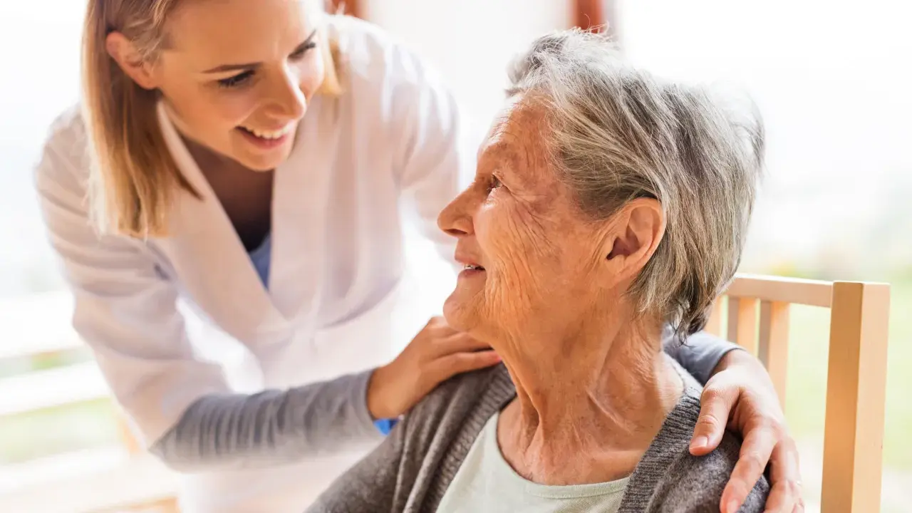 Młoda opiekunka wspiera uśmiechniętą starszą panią, która jest chora na alzheimera.