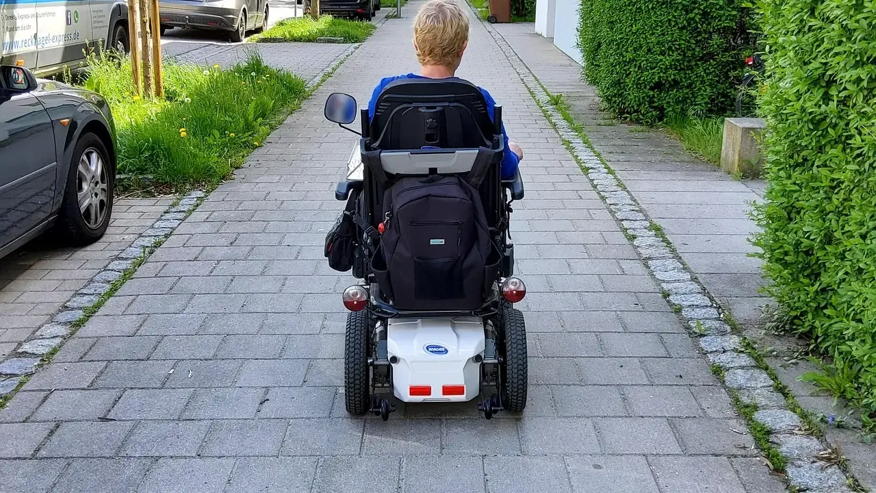 Osoba na wózku elektrycznym porusza się po chodniku. Po udarze, stopień niepełnosprawności może być różny, ale mobilność jest kluczowa.
