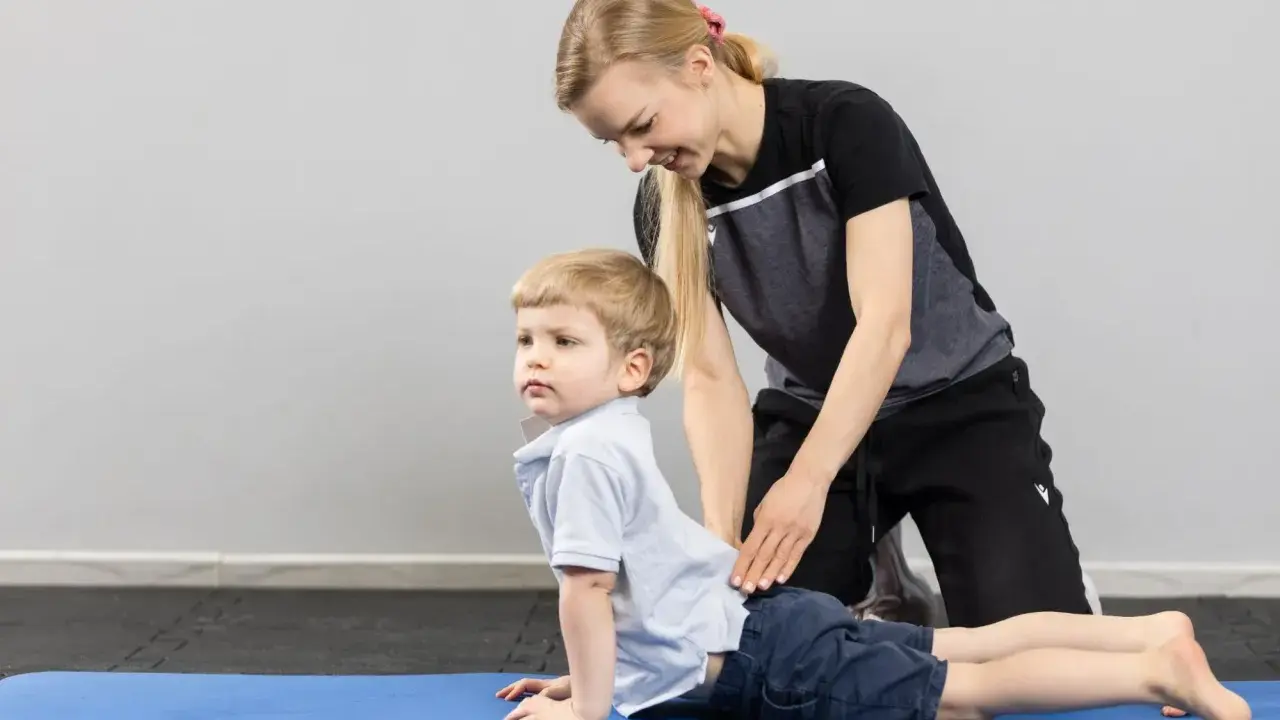 Fizjoterapeuta dziecięcy pomaga chłopcu w ćwiczeniu na macie.