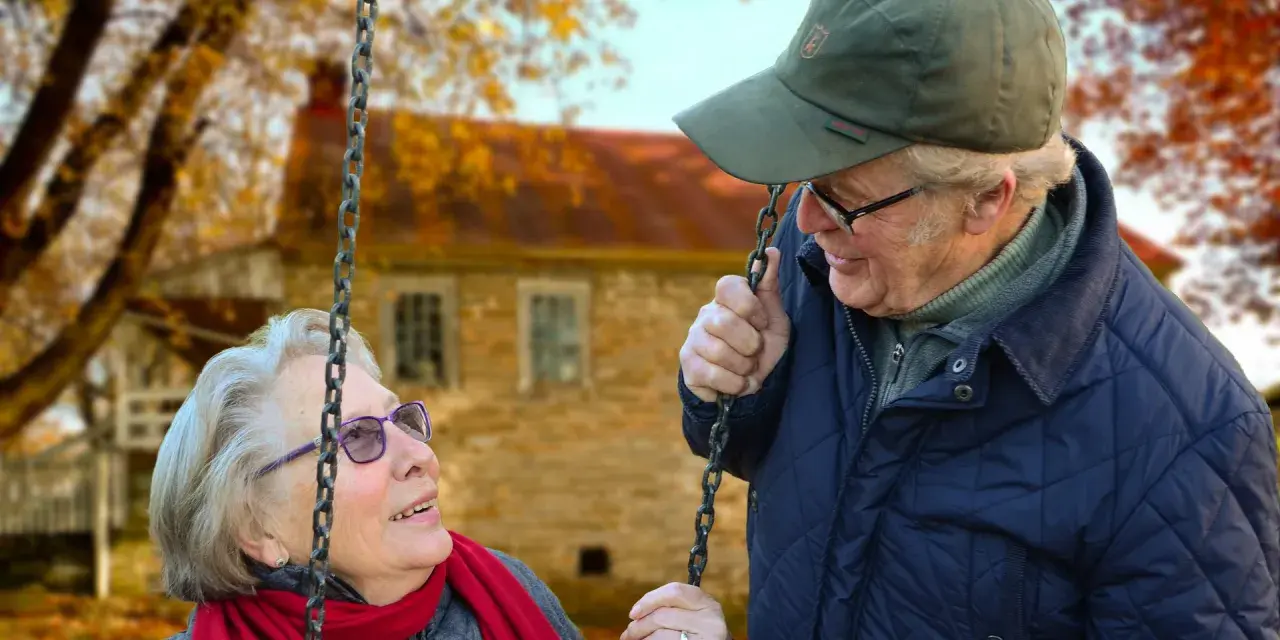 Aktywny seniorzy cieszą się jesiennym dniem na huśtawce. Uśmiechnięta para w otoczeniu złotych liści.