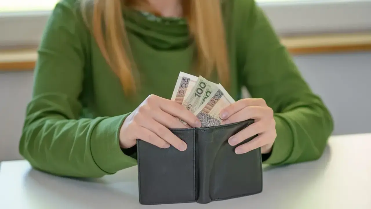 Dłoń wkłada pieniądze do portfela. Może to być wsparcie finansowe dla dziecka z orzeczeniem o niepełnosprawności.