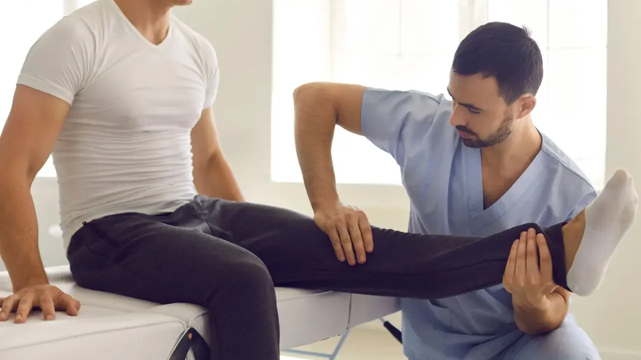 Fizjoterapeuta wykonuje zabiegi rehabilitacyjne, delikatnie unosząc nogę pacjenta.
