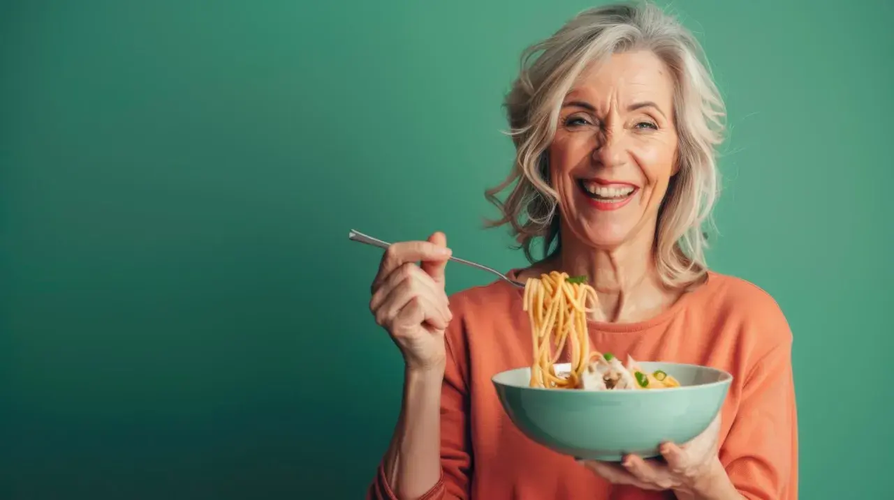 Uśmiechnięta seniorka zajada spaghetti. Pyszne danie, które pobudza co na apetyt dla seniora.