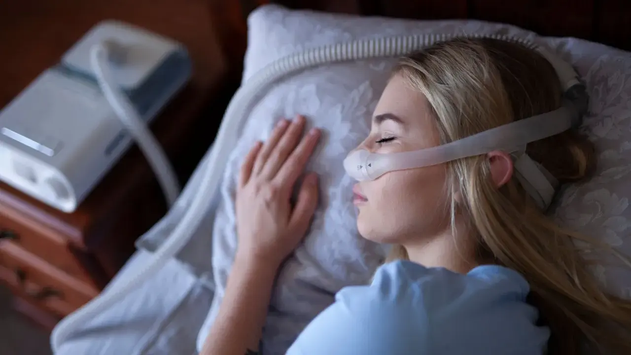Kobieta śpi z maską CPAP, która jest protezą na NFZ, zapewniając jej spokojny sen.