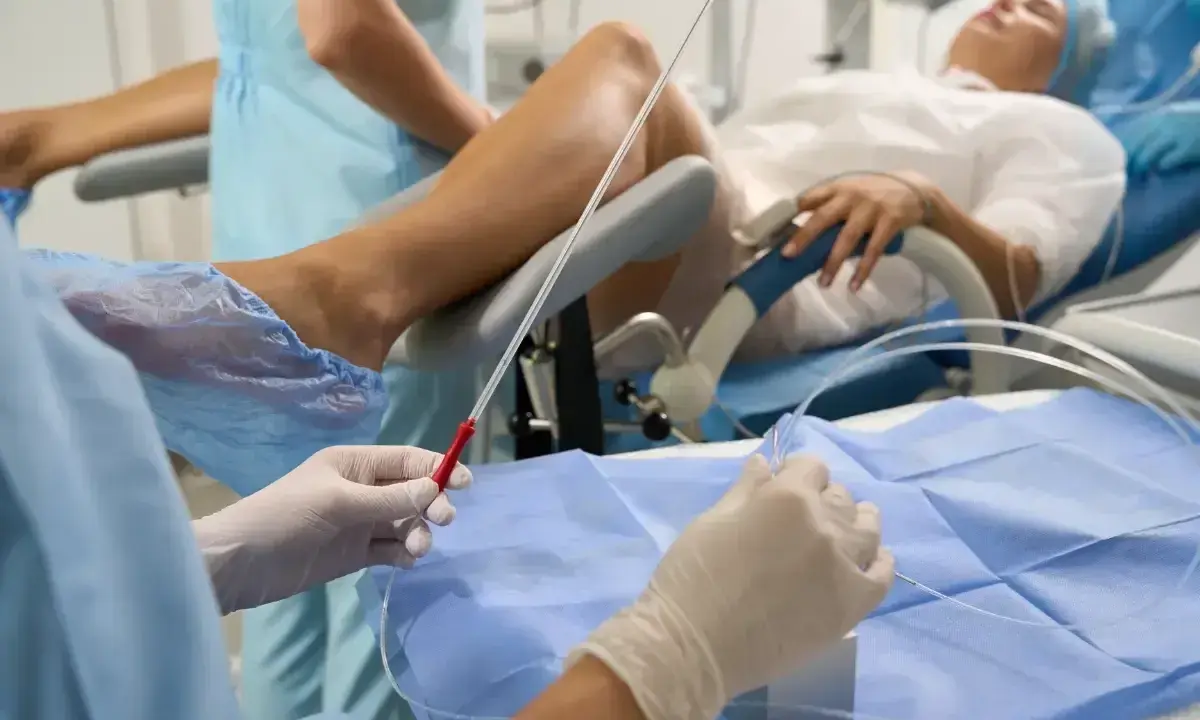 Person w rękawiczkach przygotowuje się do procedury, która może pomóc w oddawaniu moczu po wyjęciu cewnika. Pacjentka leży na łóżku.