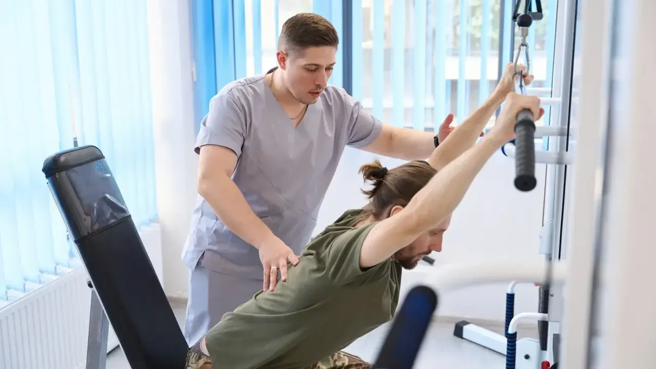 Fizjoterapeuta pomaga pacjentowi w ćwiczeniach na siłowni rehabilitacyjnej. PFRON wspiera takie działania, umożliwiając urlop rehabilitacyjny.