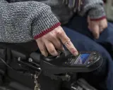 Dłoń osoby w swetrze steruje panelem wózka inwalidzkiego. Trwa naprawa wózka inwalidzkiego NFZ.
