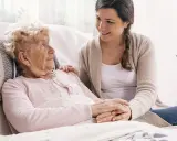 Młoda kobieta wspiera starszą panią, która może potrzebować pomocy w leczeniu alzheimera. Ich dłonie splecione są w geście troski.