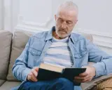 Starszy mężczyzna w okularach czyta książkę, szukając sposobów, jak poprawić pamięć.