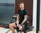 Mężczyzna w ortezie na kolanie odpoczywa po treningu. Jego rehabilitacja po operacji łąkotki przebiega pomyślnie.