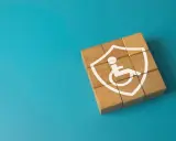 Drewniane klocki tworzą tarczę z symbolem osoby na wózku, symbolizującą ochronę w przypadku niepełnosprawności neurologicznej.