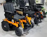 Rząd pomarańczowych i czarnych skuterów elektrycznych inwalidzkich, gotowych do naprawy lub odbioru.