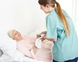Opiekunka delikatnie myje krocze starszej pacjentce, która uśmiecha się z wdzięcznością.
