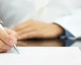 Lekarz pisze receptę farmaceutyczną, obok stoją białe opakowania leków.