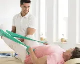 Fizjoterapeuta pomaga pacjentce w rehabilitacji poszpitalnej po endoprotezie biodra NFZ, ćwicząc nogę z taśmą oporową.