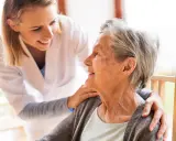 Młoda opiekunka wspiera uśmiechniętą starszą panią, która jest chora na alzheimera.