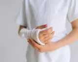 Dziecko z opuchlizną po zdjęciu gipsu nadgarstek, w białej koszulce, z ręką owiniętą bandażem.