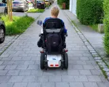 Osoba na wózku elektrycznym porusza się po chodniku. Po udarze, stopień niepełnosprawności może być różny, ale mobilność jest kluczowa.