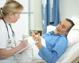Lekarka notuje, pacjent leży w łóżku. Rozmowa o tym, jak długo trwa demencja pourazowa.