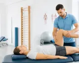 Fizjoterapeuta pracuje z pacjentką, wykonując ćwiczenia na nogę. To dowód, że rehabilitacja pomaga w powrocie do sprawności.