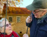 Aktywny seniorzy cieszą się jesiennym dniem na huśtawce. Uśmiechnięta para w otoczeniu złotych liści.