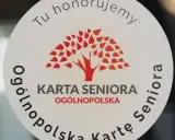 Naklejka z napisem "Tu honorujemy: KARTA SENIORA OGÓLNOPOLSKA" i drzewem. Dostępne zniżki dla posiadaczy ogólnopolskiej karty seniora.