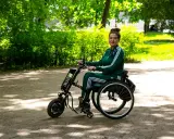 Kobieta w wózku inwalidzkim z napędem elektrycznym, który mógł zostać sfinansowany dzięki dofinansowaniu do wózka inwalidzkiego, cieszy się spacerem w parku.