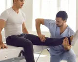 Fizjoterapeuta wykonuje zabiegi rehabilitacyjne, delikatnie unosząc nogę pacjenta.