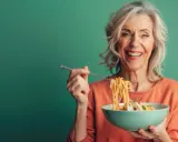 Uśmiechnięta seniorka zajada spaghetti. Pyszne danie, które pobudza co na apetyt dla seniora.