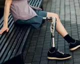 Mężczyzna z nowoczesnymi protezami nóg siedzi na ławce. Jego proteza jest zaawansowana technologicznie.