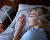 Kobieta śpi z maską CPAP, która jest protezą na NFZ, zapewniając jej spokojny sen.