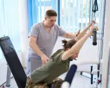 Fizjoterapeuta pomaga pacjentowi w ćwiczeniach na siłowni rehabilitacyjnej. PFRON wspiera takie działania, umożliwiając urlop rehabilitacyjny.