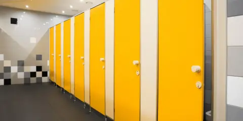 Rząd żółtych kabin w łazience, gdzie nawet wstydliwy pęcherz znajdzie chwilę spokoju.