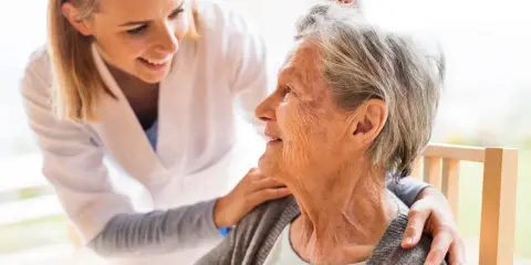 Młoda opiekunka wspiera uśmiechniętą starszą panią, która jest chora na alzheimera.