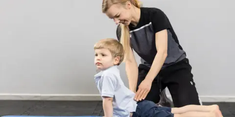 Fizjoterapeuta dziecięcy pomaga chłopcu w ćwiczeniu na macie.