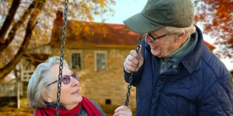 Aktywny seniorzy cieszą się jesiennym dniem na huśtawce. Uśmiechnięta para w otoczeniu złotych liści.