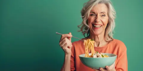 Uśmiechnięta seniorka zajada spaghetti. Pyszne danie, które pobudza co na apetyt dla seniora.