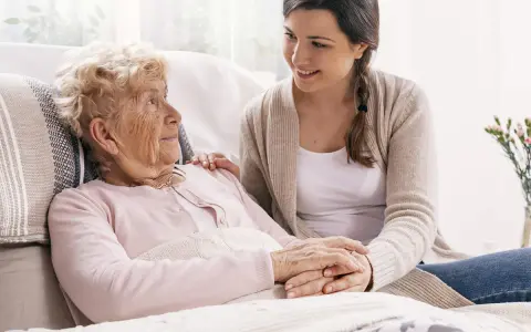 Młoda kobieta wspiera starszą panią, która może potrzebować pomocy w leczeniu alzheimera. Ich dłonie splecione są w geście troski.