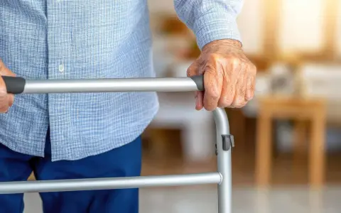 Dłoń seniora opiera się na chodziku, który może być dostępny w ramach NFZ, zapewniając wsparcie w codziennym poruszaniu się.