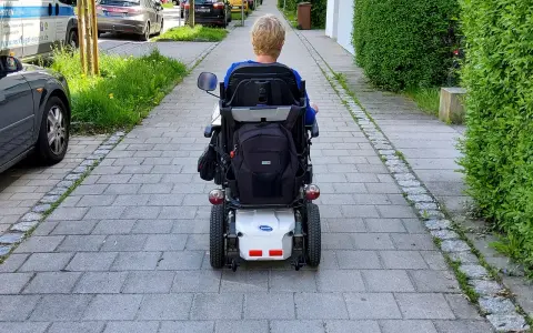Osoba na wózku elektrycznym porusza się po chodniku. Po udarze, stopień niepełnosprawności może być różny, ale mobilność jest kluczowa.