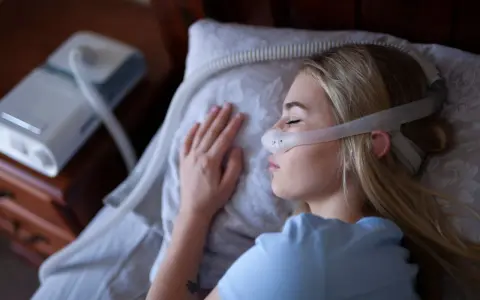 Kobieta śpi z maską CPAP, która jest protezą na NFZ, zapewniając jej spokojny sen.