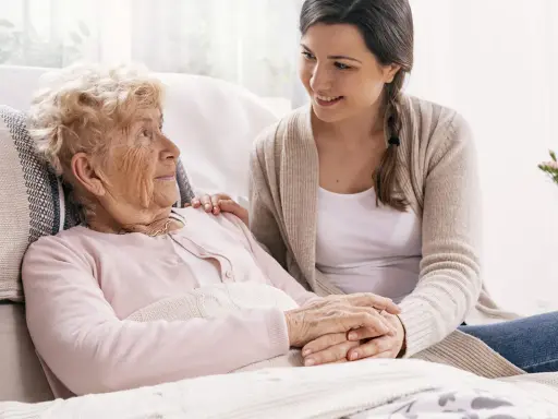 Młoda kobieta wspiera starszą panią, która może potrzebować pomocy w leczeniu alzheimera. Ich dłonie splecione są w geście troski.