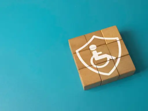 Drewniane klocki tworzą tarczę z symbolem osoby na wózku, symbolizującą ochronę w przypadku niepełnosprawności neurologicznej.