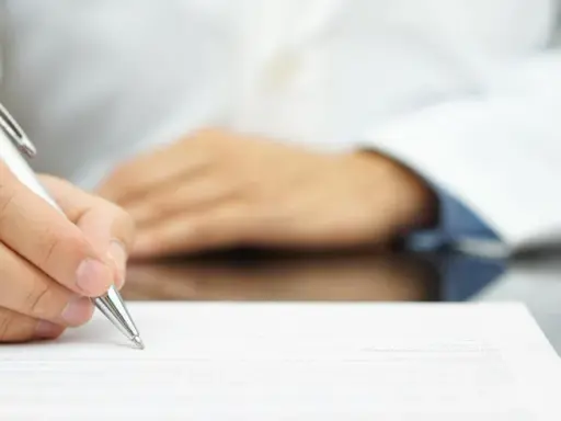 Lekarz pisze receptę farmaceutyczną, obok stoją białe opakowania leków.