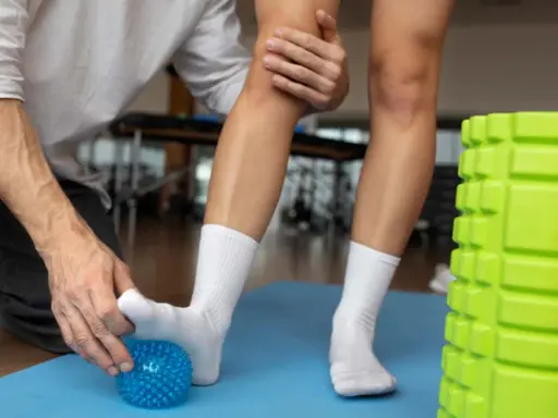 Fizjoterapeuta pomaga pacjentowi z lekkim skręceniem kostki, masując stopę kolczastą piłeczką.