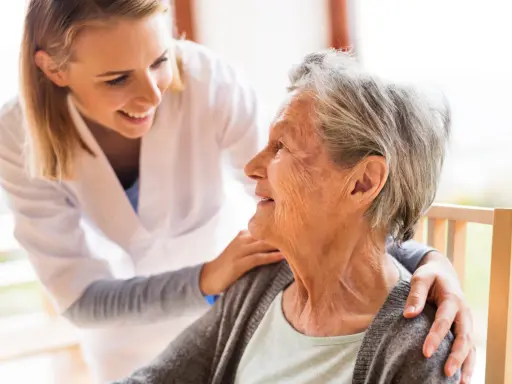Młoda opiekunka wspiera uśmiechniętą starszą panią, która jest chora na alzheimera.