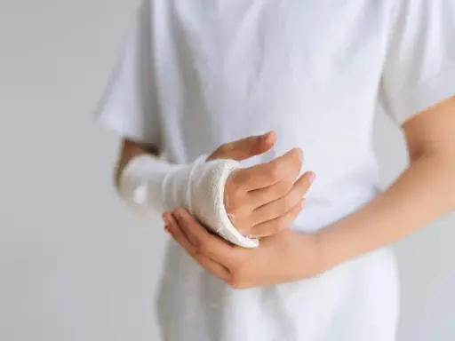 Dziecko z opuchlizną po zdjęciu gipsu nadgarstek, w białej koszulce, z ręką owiniętą bandażem.