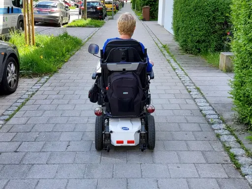 Osoba na wózku elektrycznym porusza się po chodniku. Po udarze, stopień niepełnosprawności może być różny, ale mobilność jest kluczowa.